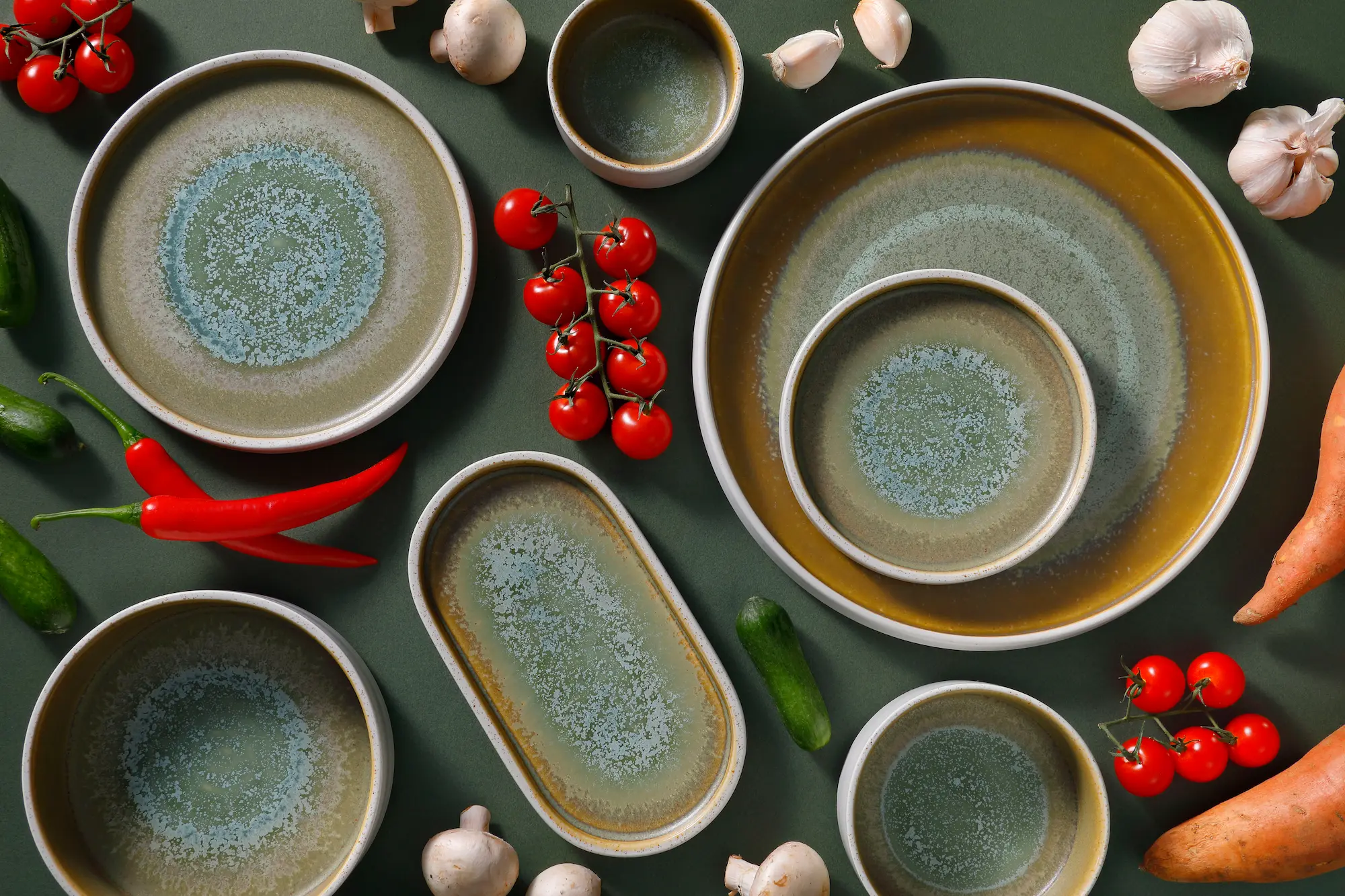 Ceramic plates, bowls, and platters with green and brown glaze on a dark green surface